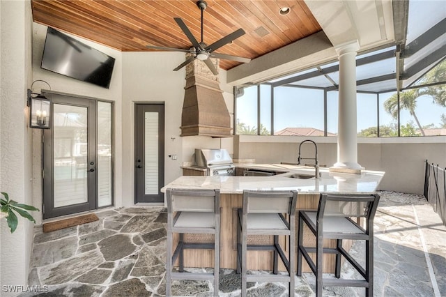 view of patio / terrace with glass enclosure, outdoor wet bar, a sink, a ceiling fan, and exterior kitchen