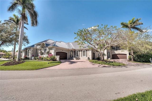 mediterranean / spanish house with a garage, decorative driveway, a front lawn, and stucco siding