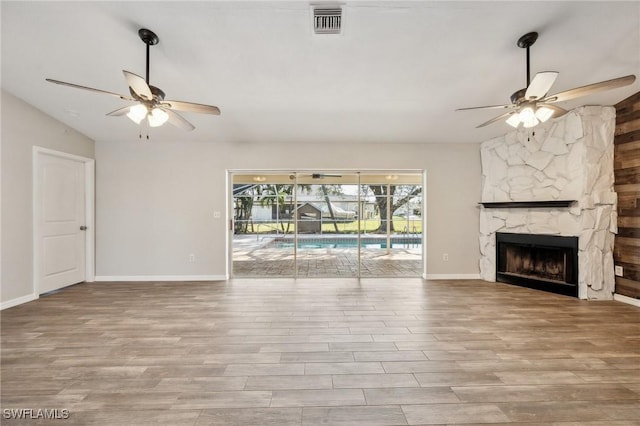 unfurnished living room featuring ceiling fan, a fireplace, visible vents, and wood finished floors