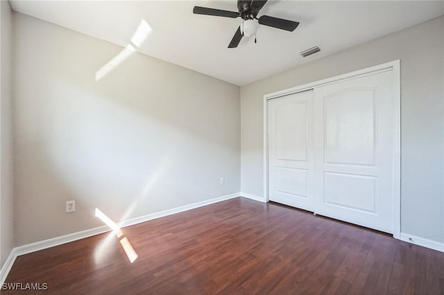 unfurnished bedroom with dark wood-type flooring, a closet, visible vents, and baseboards