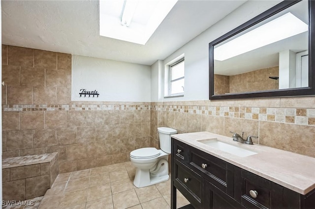 full bathroom featuring a skylight, toilet, tile patterned floors, vanity, and tile walls