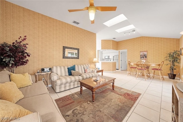 living room featuring light tile patterned floors, visible vents, ceiling fan, vaulted ceiling with skylight, and wallpapered walls