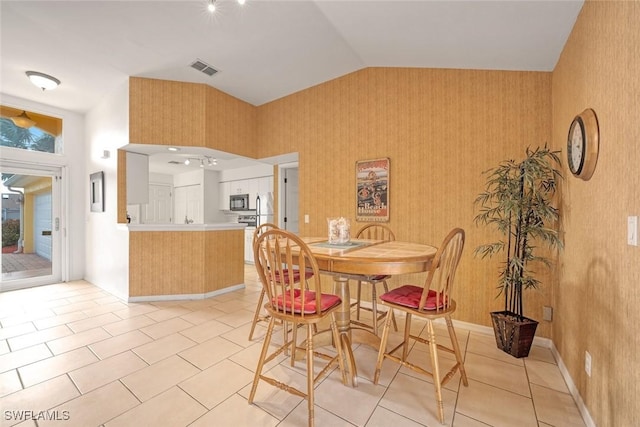 dining room featuring light tile patterned floors, lofted ceiling, visible vents, baseboards, and wallpapered walls