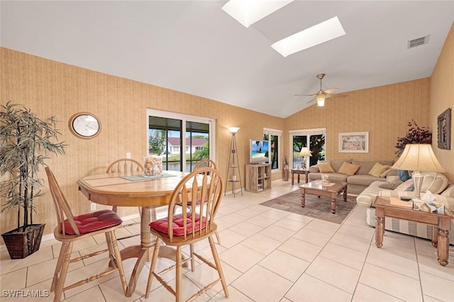 dining space with ceiling fan, light tile patterned floors, visible vents, lofted ceiling with skylight, and wallpapered walls