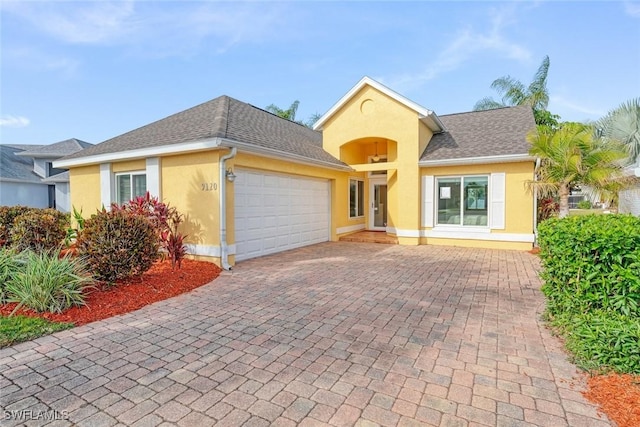 ranch-style home with a shingled roof, decorative driveway, an attached garage, and stucco siding