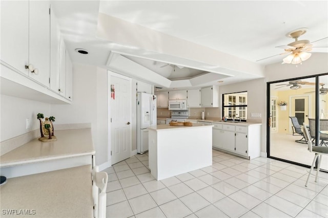 kitchen featuring white appliances, white cabinets, a raised ceiling, light countertops, and a sink