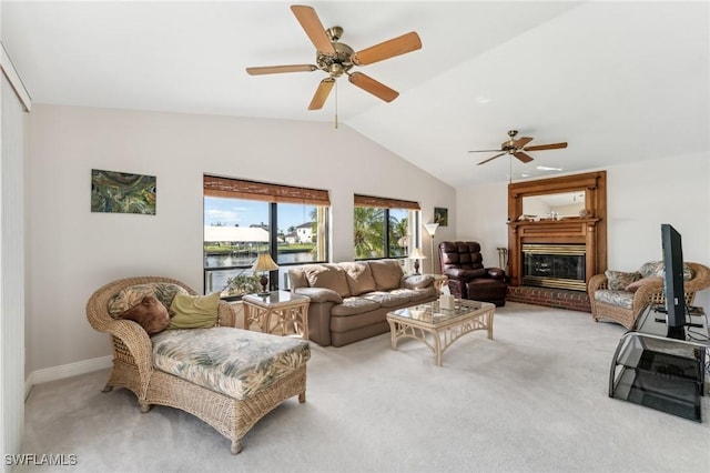 living area with lofted ceiling, a glass covered fireplace, a ceiling fan, and light colored carpet