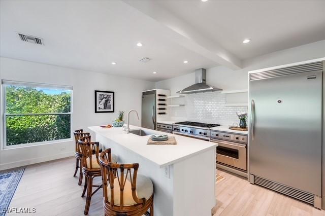 kitchen featuring visible vents, wall chimney exhaust hood, oven, built in refrigerator, and a sink