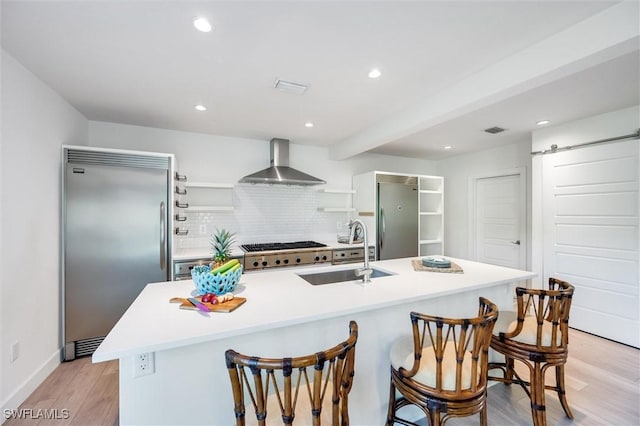 kitchen with a barn door, wall chimney range hood, built in refrigerator, and a sink