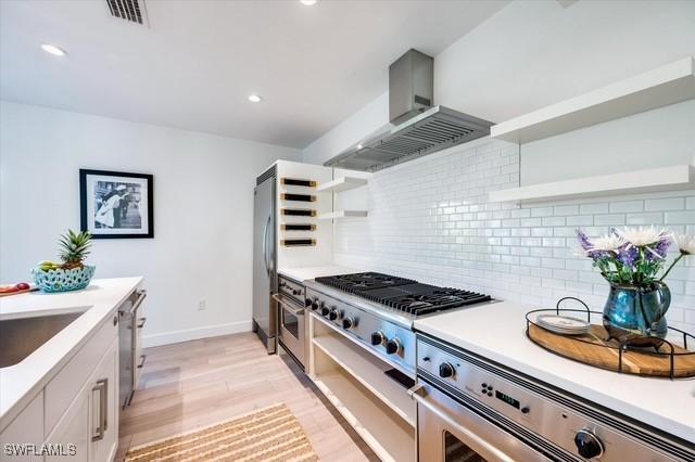 kitchen with open shelves, stainless steel appliances, visible vents, decorative backsplash, and wall chimney range hood