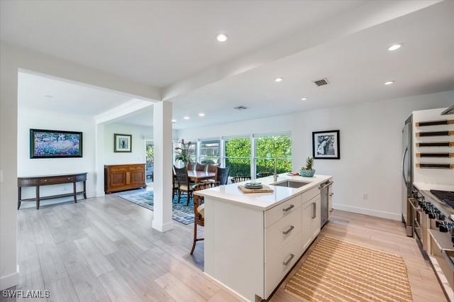 kitchen with stainless steel dishwasher, a center island with sink, and light wood-style flooring