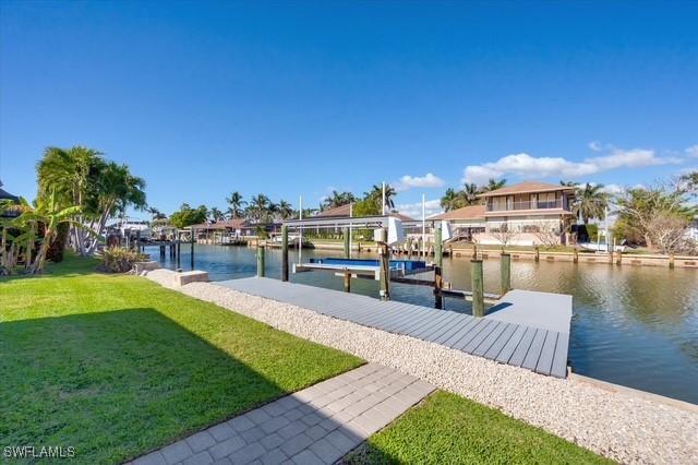 dock area with a water view, boat lift, and a lawn