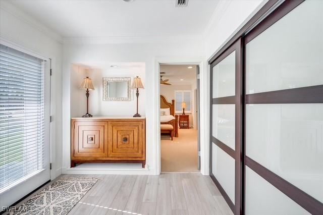 corridor featuring light wood finished floors, visible vents, and crown molding