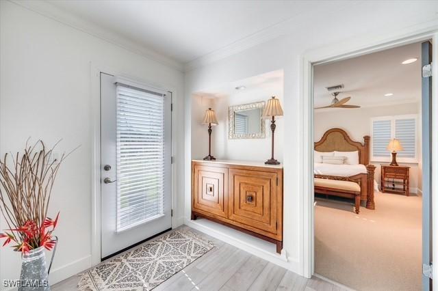 doorway with baseboards, light wood-type flooring, and crown molding