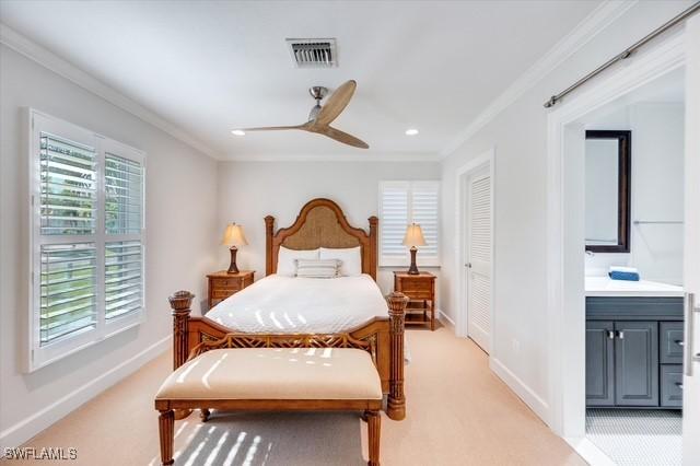 bedroom featuring light carpet, visible vents, baseboards, ornamental molding, and ensuite bath