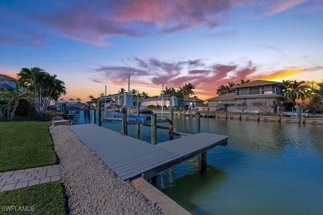 dock area featuring a water view, boat lift, and a lawn