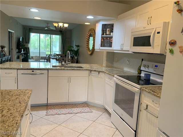 kitchen featuring light tile patterned floors, a sink, light stone countertops, white appliances, and a peninsula