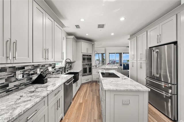 kitchen with stainless steel appliances, a sink, backsplash, a center island, and light wood finished floors