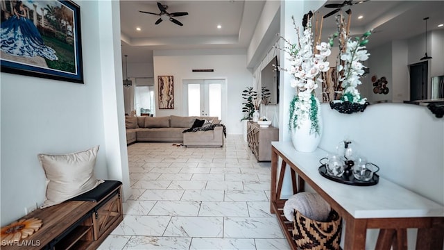 corridor with a tray ceiling, marble finish floor, french doors, and recessed lighting