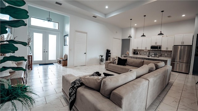 living area featuring a towering ceiling, marble finish floor, visible vents, and french doors