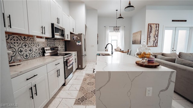 kitchen with a center island with sink, appliances with stainless steel finishes, open floor plan, a sink, and backsplash