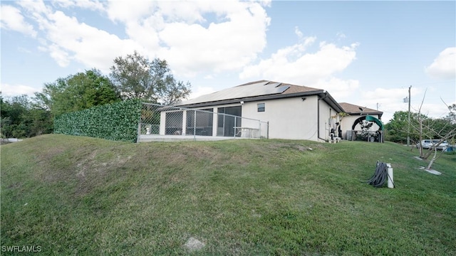 back of property with roof mounted solar panels, a lawn, and stucco siding