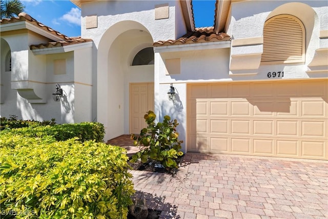 mediterranean / spanish-style house with decorative driveway, a tiled roof, an attached garage, and stucco siding