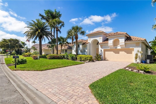 mediterranean / spanish-style house featuring an attached garage, a tile roof, decorative driveway, stucco siding, and a front lawn