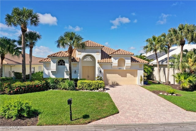 mediterranean / spanish-style house with a garage, a tile roof, decorative driveway, stucco siding, and a front lawn