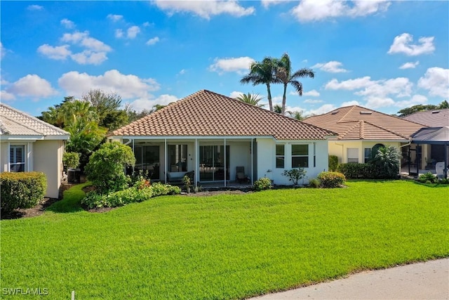 back of property with a sunroom, a tile roof, a lawn, and stucco siding