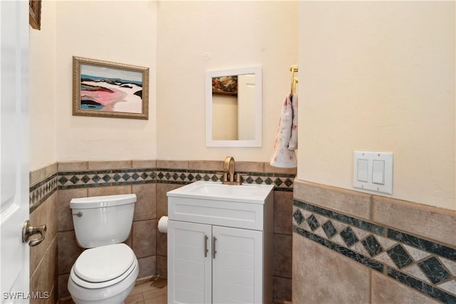 bathroom with wainscoting, vanity, toilet, and tile walls