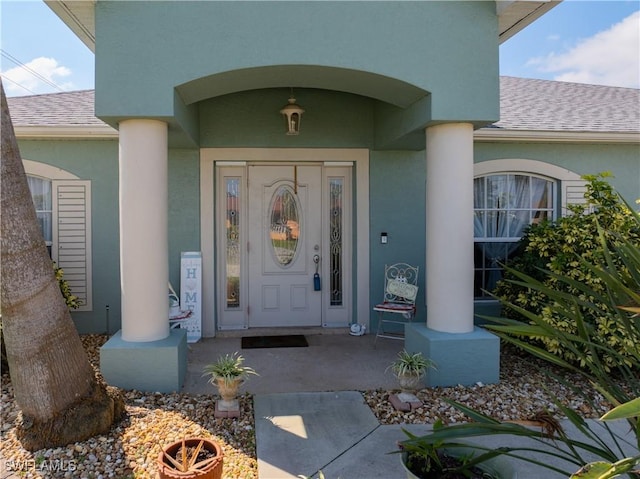 view of exterior entry with a shingled roof and stucco siding