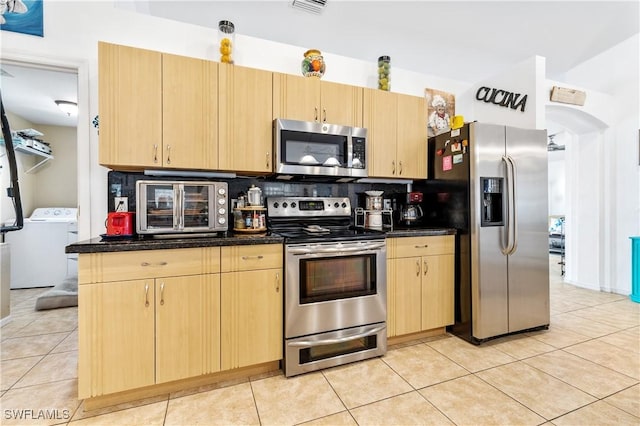 kitchen with light tile patterned floors, appliances with stainless steel finishes, backsplash, light brown cabinetry, and washer / clothes dryer