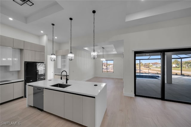 kitchen with a center island with sink, a raised ceiling, a sink, modern cabinets, and black appliances