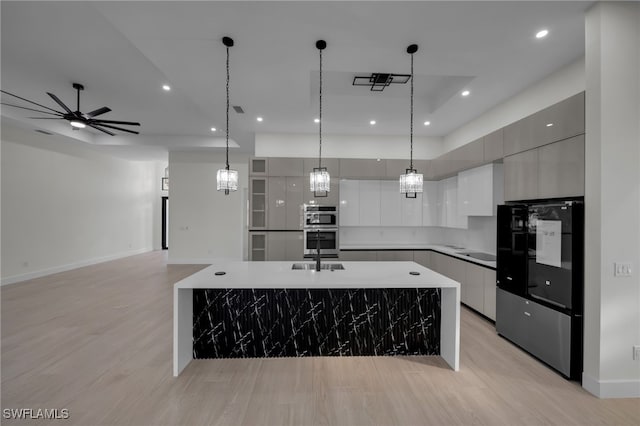 kitchen featuring modern cabinets, decorative light fixtures, a kitchen island with sink, double oven, and white cabinetry