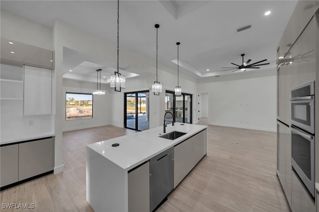 kitchen with a sink, open floor plan, appliances with stainless steel finishes, modern cabinets, and a raised ceiling