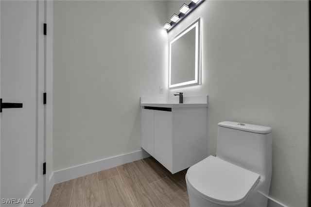 half bath featuring baseboards, vanity, toilet, and wood finished floors