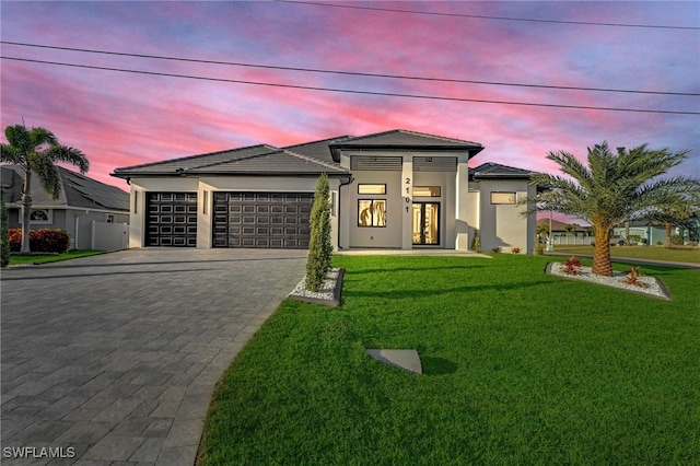 prairie-style home with a front lawn, decorative driveway, an attached garage, and stucco siding