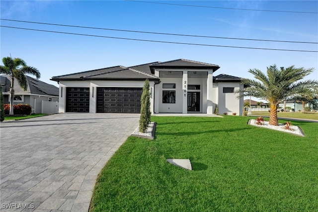 prairie-style home with a garage, decorative driveway, a front lawn, and stucco siding