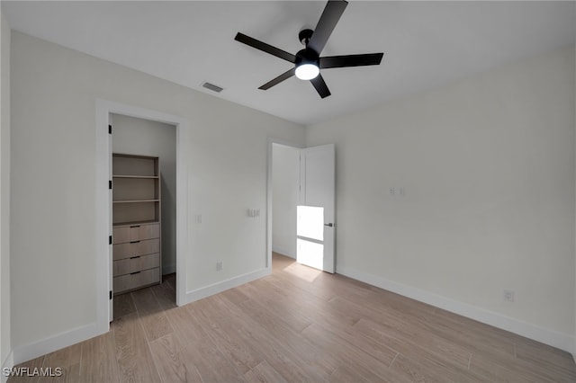 unfurnished bedroom with light wood finished floors, visible vents, baseboards, a ceiling fan, and a spacious closet