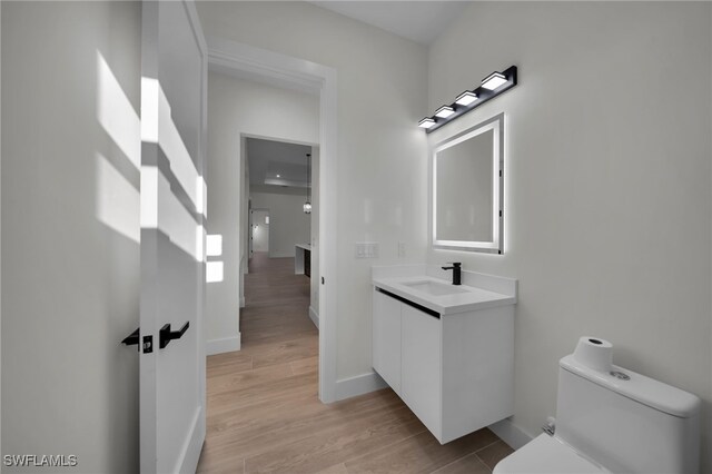 bathroom featuring toilet, baseboards, wood finished floors, and vanity