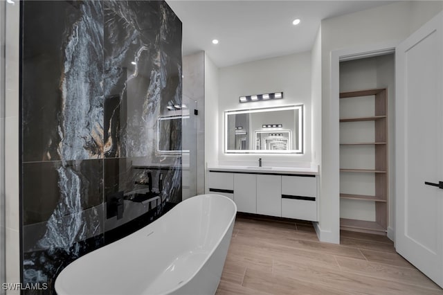 bathroom with wood finish floors, a marble finish shower, recessed lighting, a freestanding bath, and vanity