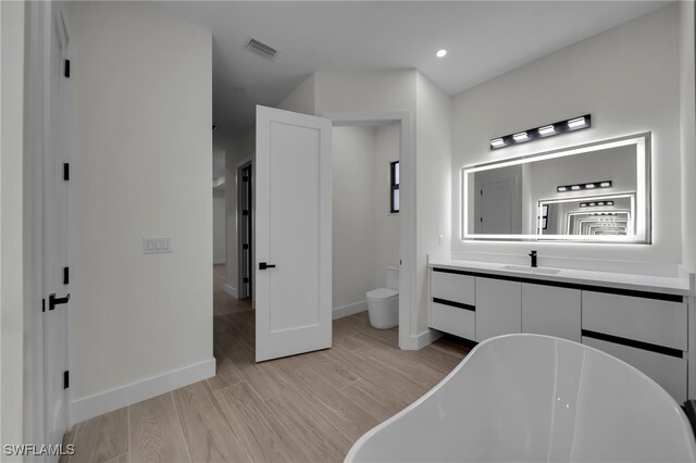 full bath featuring visible vents, toilet, a soaking tub, wood finished floors, and vanity