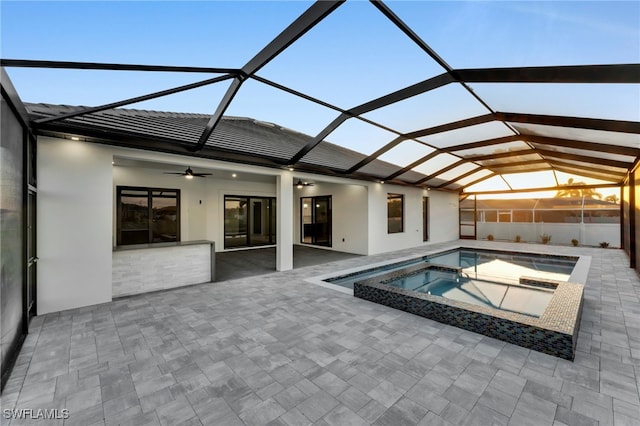 view of swimming pool featuring ceiling fan, glass enclosure, a patio area, and a pool with connected hot tub