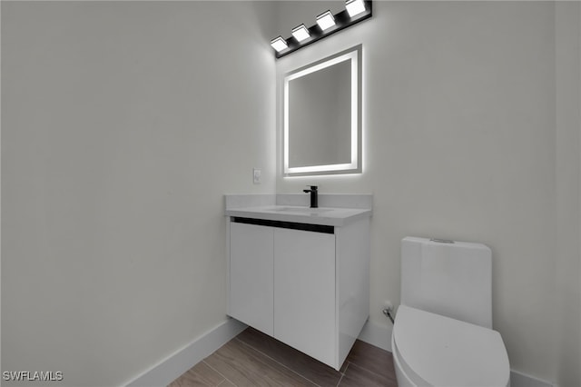 bathroom with toilet, wood finished floors, vanity, and baseboards