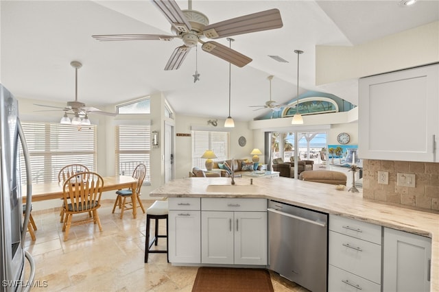 kitchen with a sink, appliances with stainless steel finishes, a peninsula, decorative backsplash, and lofted ceiling