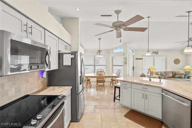 kitchen with ceiling fan, stone tile flooring, a sink, appliances with stainless steel finishes, and tasteful backsplash