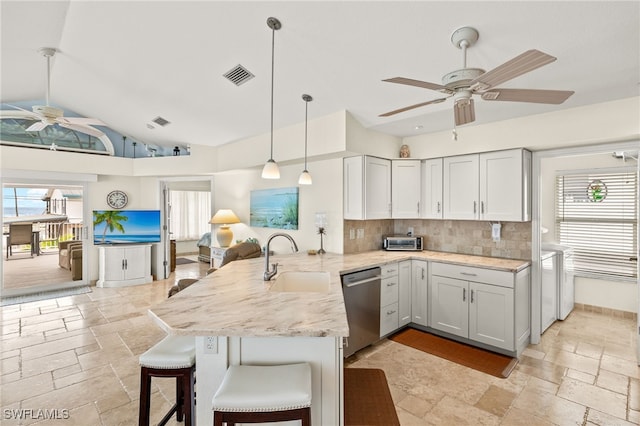 kitchen featuring visible vents, dishwasher, a peninsula, stone tile flooring, and a sink