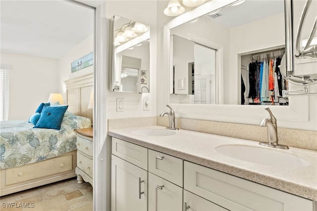 ensuite bathroom with double vanity, visible vents, stone finish flooring, and a sink