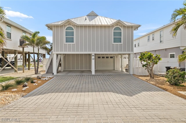 coastal home with decorative driveway, board and batten siding, metal roof, a carport, and stairs